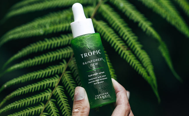 Tropic Rainforest Dew skincare serum held in front of green leaves